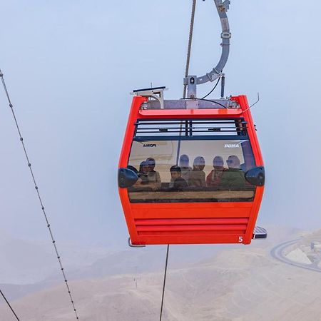 Tolip Resort El Galala Majestic Ain Sukhna Dış mekan fotoğraf The photo shows a red gondola lift suspended in the air, traveling along cables. Inside the gondola, a group of people can be seen. The background features a hazy landscape, possibly mountains or hills, indicating an elevated area. The scene conveys 
