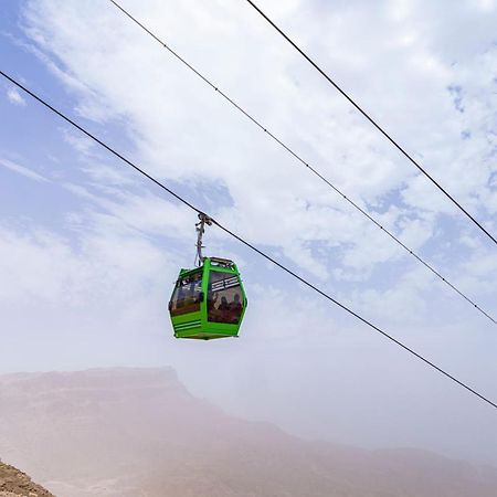 Tolip Resort El Galala Majestic Ain Sukhna Dış mekan fotoğraf The photo shows a green cable car suspended in the air, traveling along overhead cables. The backdrop features a hazy landscape, likely mountainous or elevated terrain, with a cloudy sky. The scene suggests a scenic transportation method, possibly us