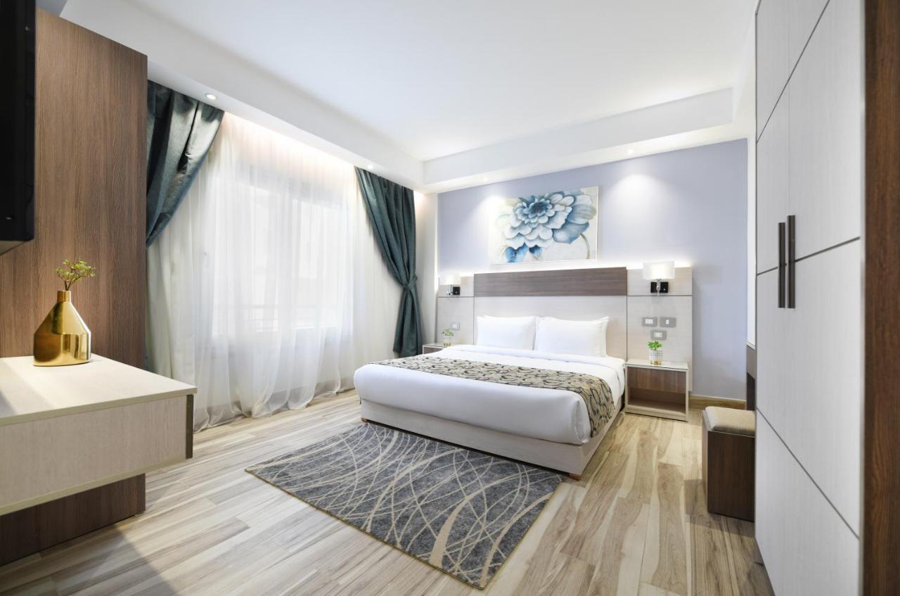 Tolip Resort El Galala Majestic Ain Sukhna Dış mekan fotoğraf The photo shows a modern bedroom with a clean and stylish design. It features a large bed with white bedding positioned against a wall. Above the bed, there is a decorative artwork, possibly a floral design. The room has large windows with sheer curt