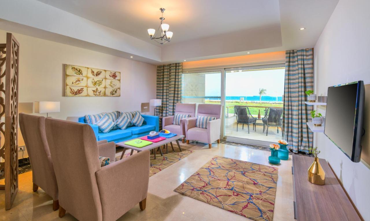Tolip Resort El Galala Majestic Ain Sukhna Dış mekan fotoğraf The photo shows a bright and modern living room. It features a blue sofa with decorative cushions, two light-colored armchairs, and a coffee table. A large area rug adds warmth to the space, which is decorated with a subtle pattern. The walls have so