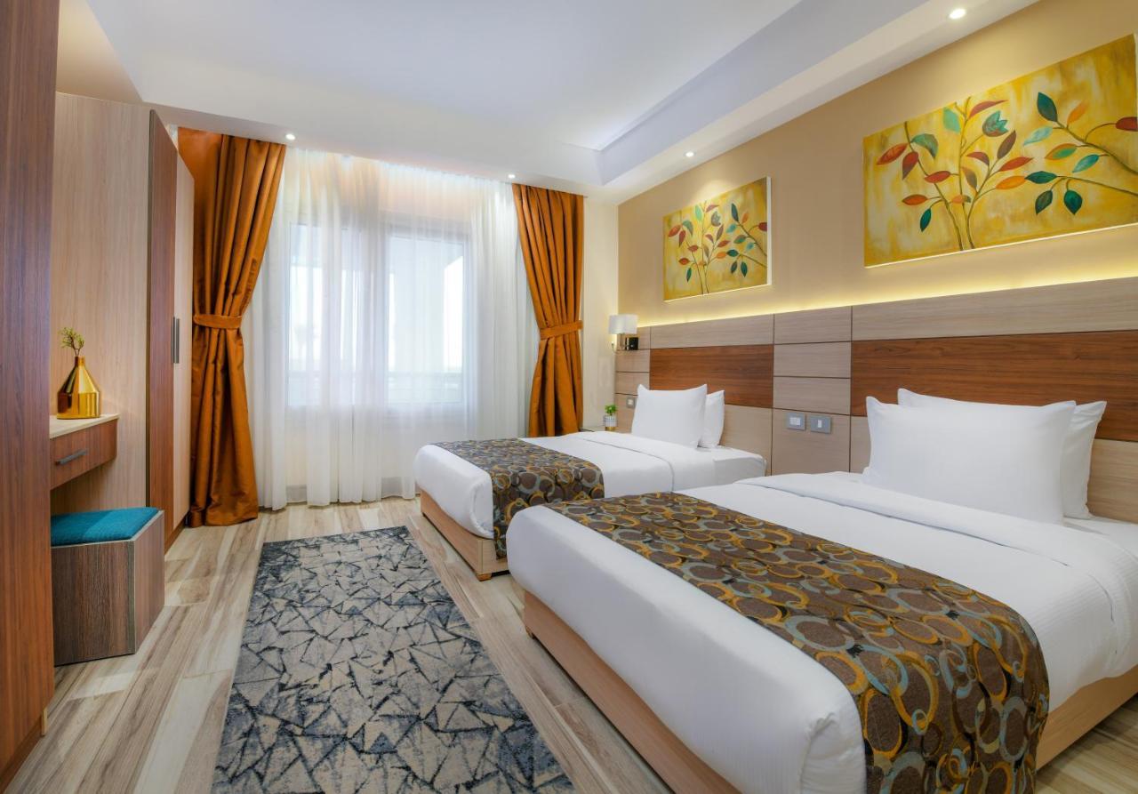 Tolip Resort El Galala Majestic Ain Sukhna Dış mekan fotoğraf The photo shows a modern hotel room with two single beds, each covered with white linens and decorative brown bed throws. The walls are painted in warm colors, and there are two pieces of artwork featuring floral and leaf designs above the beds. The 