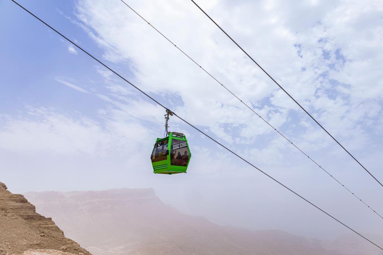 Tolip Resort El Galala Majestic Ain Sukhna Dış mekan fotoğraf The photo shows a green cable car suspended in the air, traveling along overhead cables. The backdrop features a hazy landscape, likely mountainous or elevated terrain, with a cloudy sky. The scene suggests a scenic transportation method, possibly us