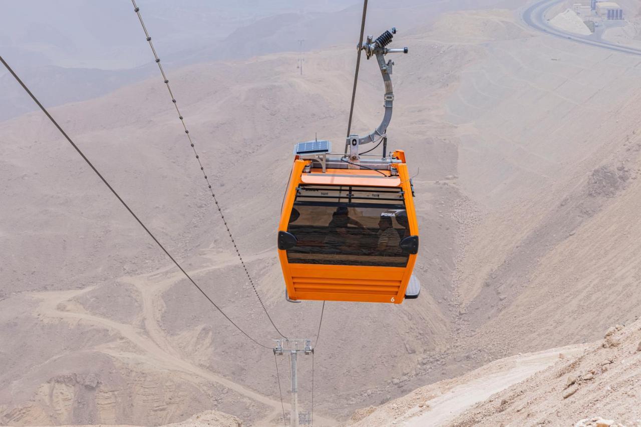Tolip Resort El Galala Majestic Ain Sukhna Dış mekan fotoğraf The photo shows an orange cable car suspended in the air, traveling along a set of cables. It appears to be located in a mountainous or hilly area, with rugged terrain and dry, rocky landscapes visible below. The background features slopes that seem 