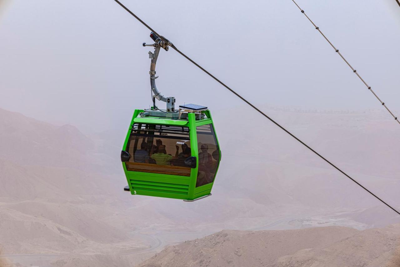 Tolip Resort El Galala Majestic Ain Sukhna Dış mekan fotoğraf The photo shows a green cable car suspended in the air, moving along a wire. The cable car appears to be traversing a mountainous landscape, which looks rocky and arid. The surrounding environment is somewhat foggy or hazy, suggesting limited visibil