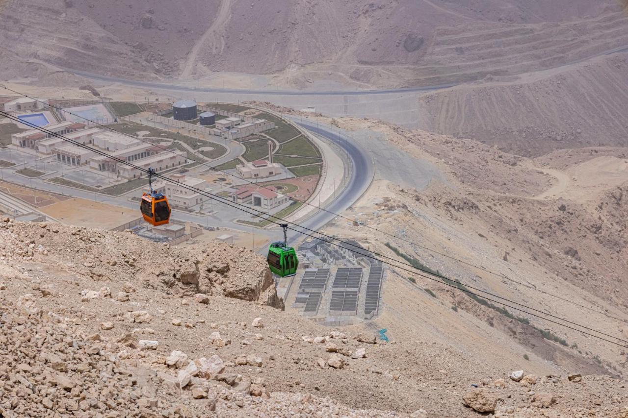 Tolip Resort El Galala Majestic Ain Sukhna Dış mekan fotoğraf The photo shows a scenic view from a high elevation, featuring a cable car system. Two cable cars are visible, one orange and one green, traveling along cables down the mountainside. Below, there appears to be a developed area with roads and light st