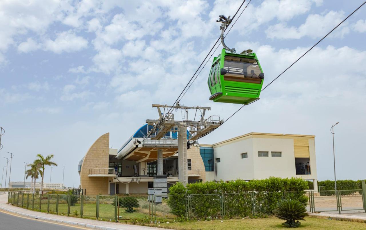 Tolip Resort El Galala Majestic Ain Sukhna Dış mekan fotoğraf The photo shows a cable car or gondola system in operation, featuring a green-colored gondola. It is suspended from cables and moving towards a station, which appears to be a modern building with a unique architectural design. The station has large w