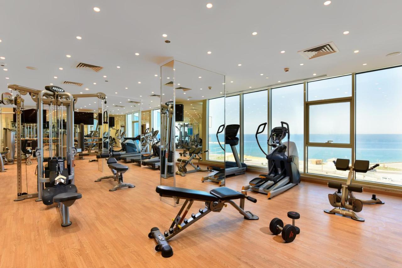 Tolip Resort El Galala Majestic Ain Sukhna Dış mekan fotoğraf The photo shows a modern gym interior with a variety of fitness equipment. There are cardio machines like treadmills and ellipticals, along with strength training equipment such as free weights and benches. The gym features large windows that offer a