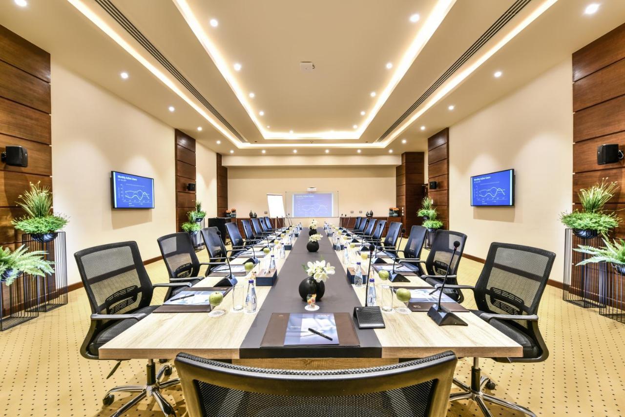 Tolip Resort El Galala Majestic Ain Sukhna Dış mekan fotoğraf The photo shows a modern conference room designed for meetings. It features a long rectangular table at the center, surrounded by ergonomic black chairs. The room is well-lit with ceiling lights and has a neutral color scheme. There are two large scr