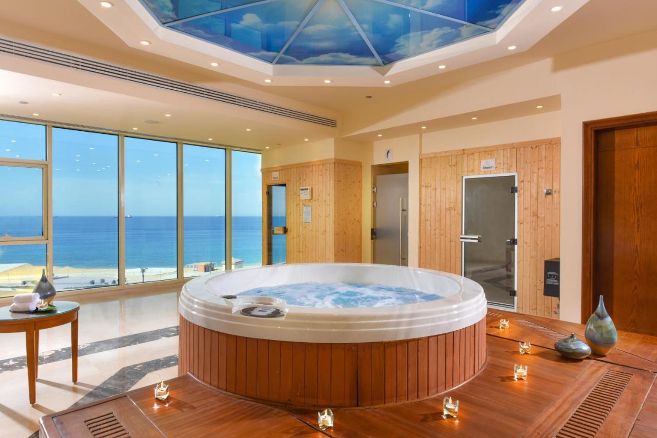 Tolip Resort El Galala Majestic Ain Sukhna Dış mekan fotoğraf The photo shows a luxurious spa room featuring a large, round hot tub positioned in the center. The walls are mostly glass, offering a stunning view of the ocean. The ceiling has a painted sky, enhancing the serene atmosphere. There are wooden elemen