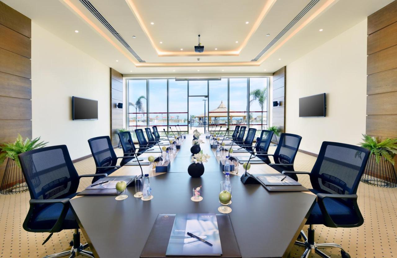 Tolip Resort El Galala Majestic Ain Sukhna Dış mekan fotoğraf The image shows a modern conference room with a large, dark rectangular table surrounded by ergonomic black chairs. The room features large windows that allow natural light to enter and provide a view of the outdoors, including some greenery. On the 