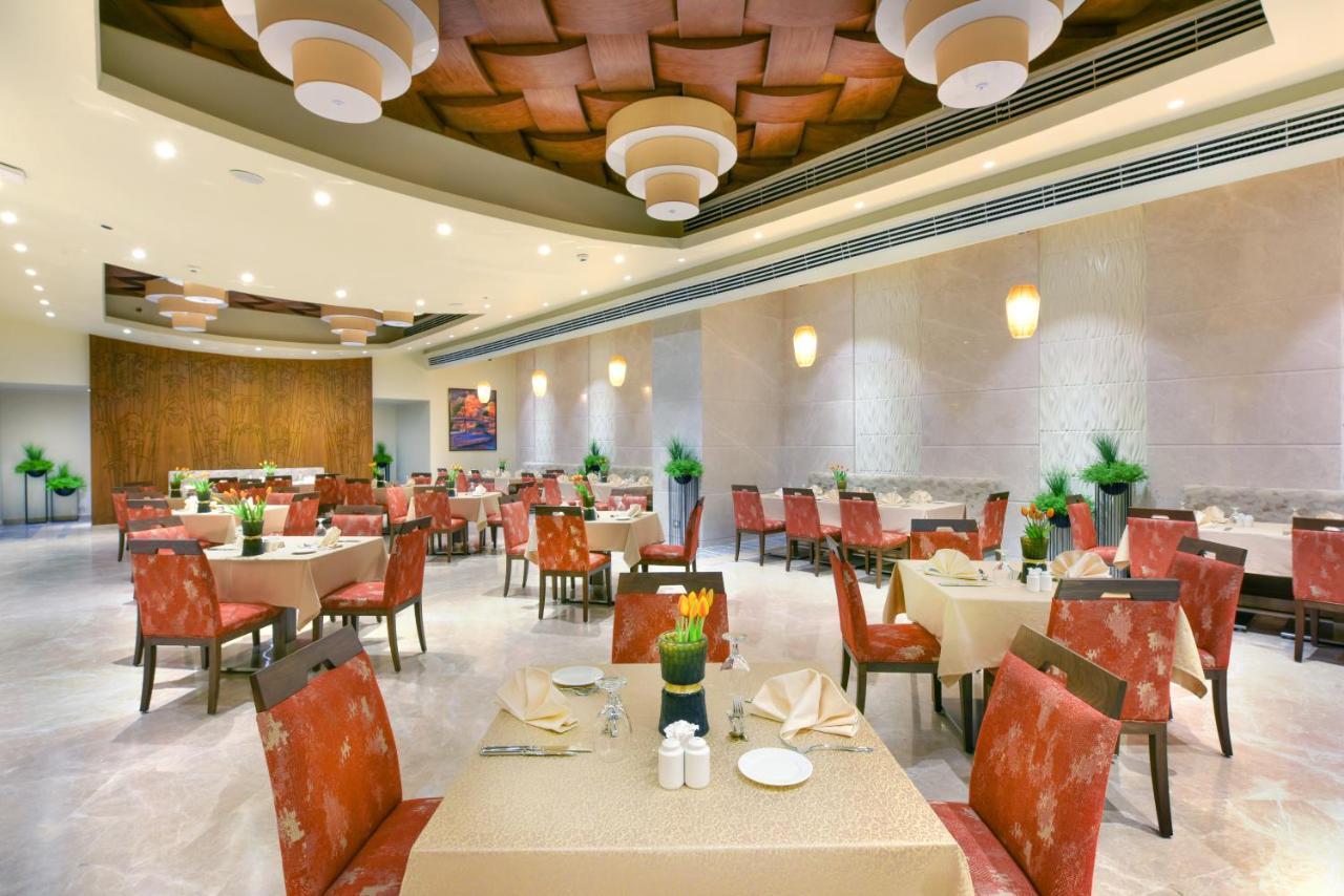Tolip Resort El Galala Majestic Ain Sukhna Dış mekan fotoğraf The photo shows the interior of a restaurant. The space features several tables set with light-colored tablecloths and chairs with reddish upholstery. Each table is adorned with decorative napkins and has small plants in the center. The room has a mo