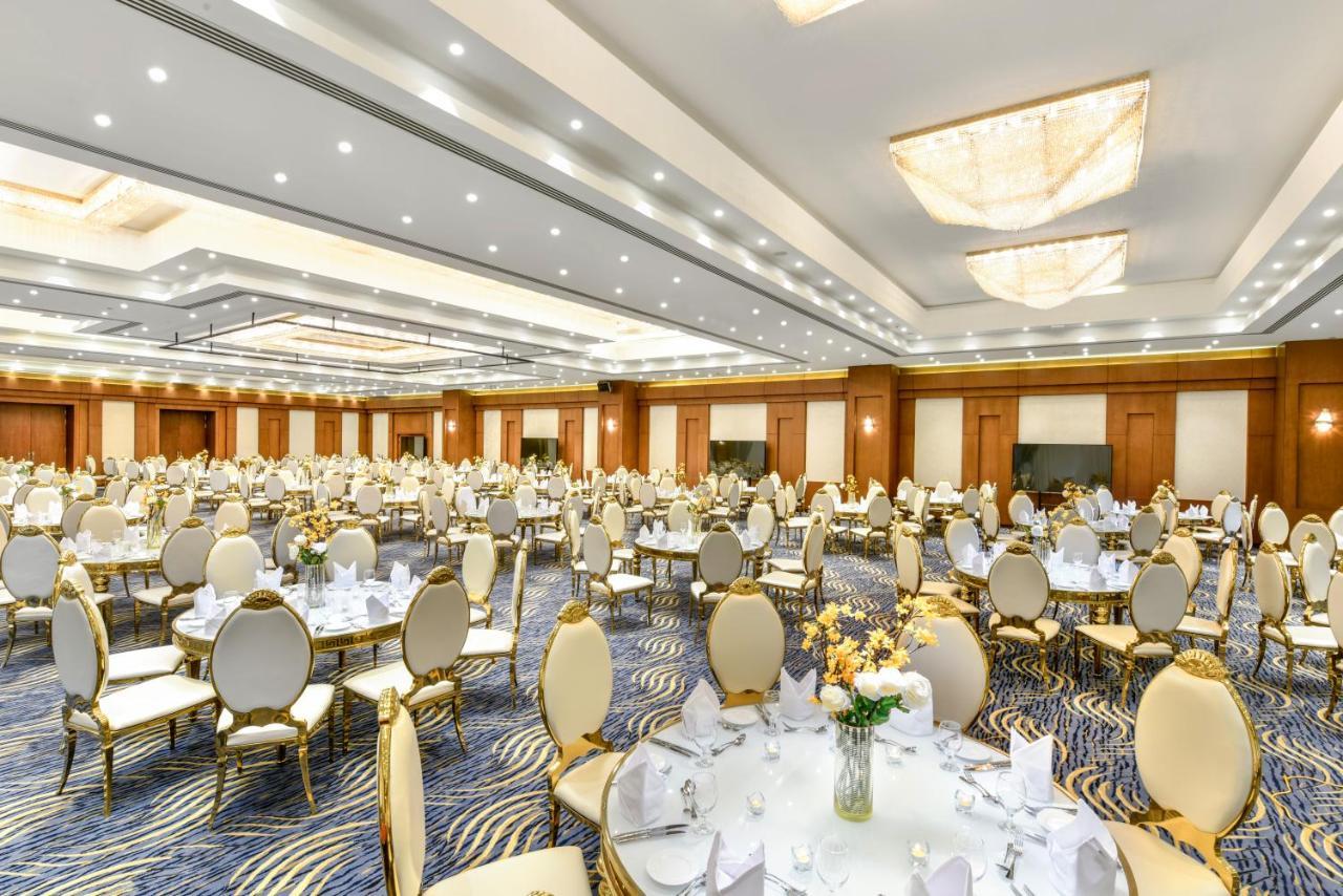 Tolip Resort El Galala Majestic Ain Sukhna Dış mekan fotoğraf The photo shows a spacious and elegantly decorated banquet hall. The room features numerous round dining tables, each set with white tablecloths and adorned with decorative centerpieces, likely flowers. The chairs surrounding the tables have a luxuri
